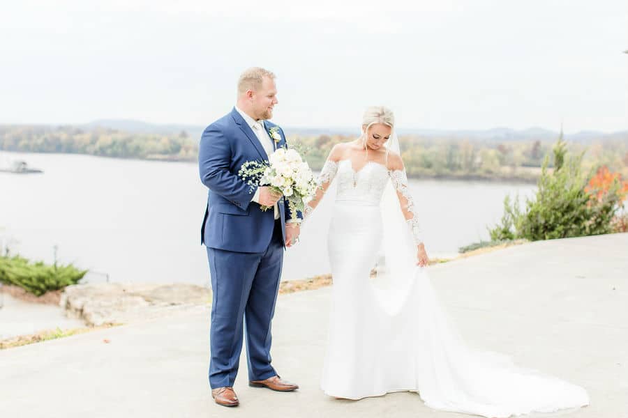 The bride walks with the groom on a path by the river