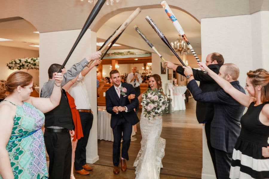 Bride and groom walk under an arch of baseball bats
