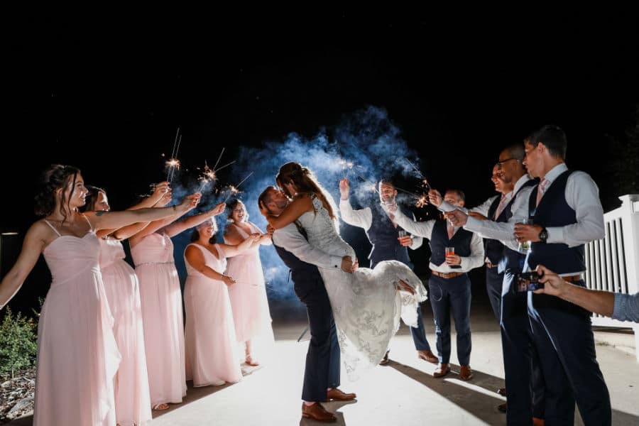 Bride and groom kiss in front of sparklers held by the wedding party