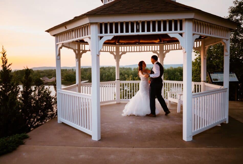 Bride and Groom dancing in a white gazebo on th eriver bluff. He doesn't have his coat of his three piece suit.