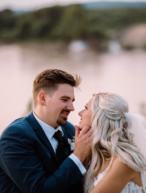 Man in navy blue suit holding the face of a woman in a white dress