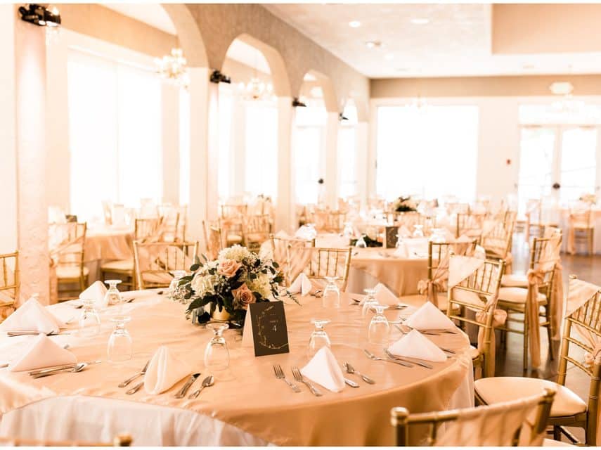 Large reception hall set up with tables with white linens, gold chairs, and large bouquets of flowers