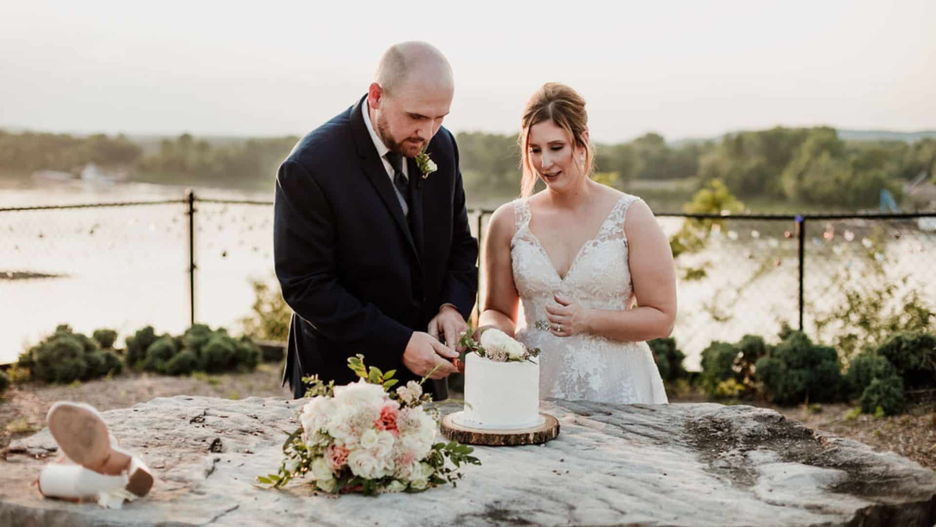 bride and groom cutting their wedding cake on herman hill’s river bluff with locks of love fence in the background