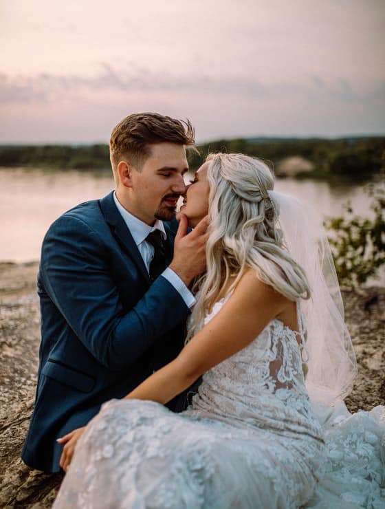 Lady in white dress and man in blue suit sitting on a rock with a river in the background