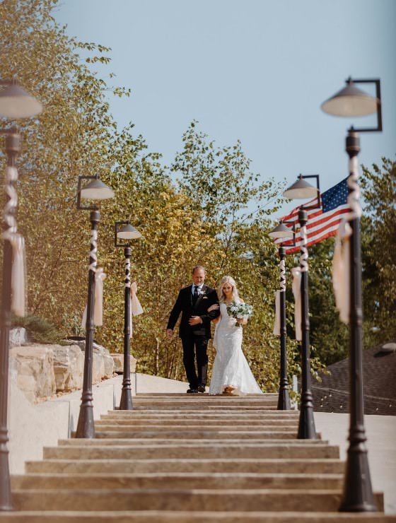 Lady in white dress holding arm of man in black suit walking down steps