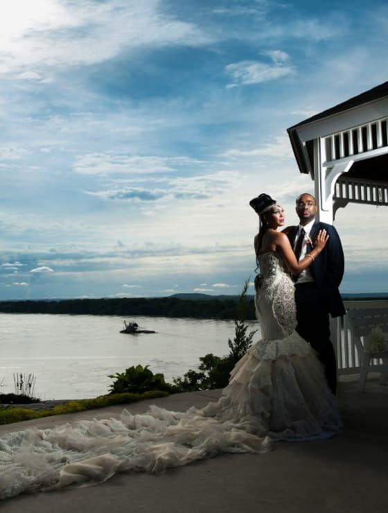Lady in white dress standing by man in black suit with river in the background