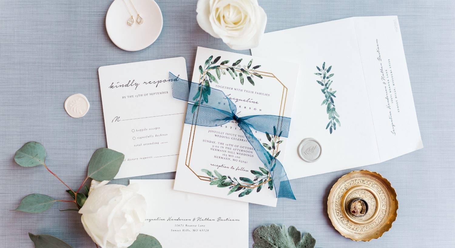 All pieces of a wedding invitation spread out on blue fabric