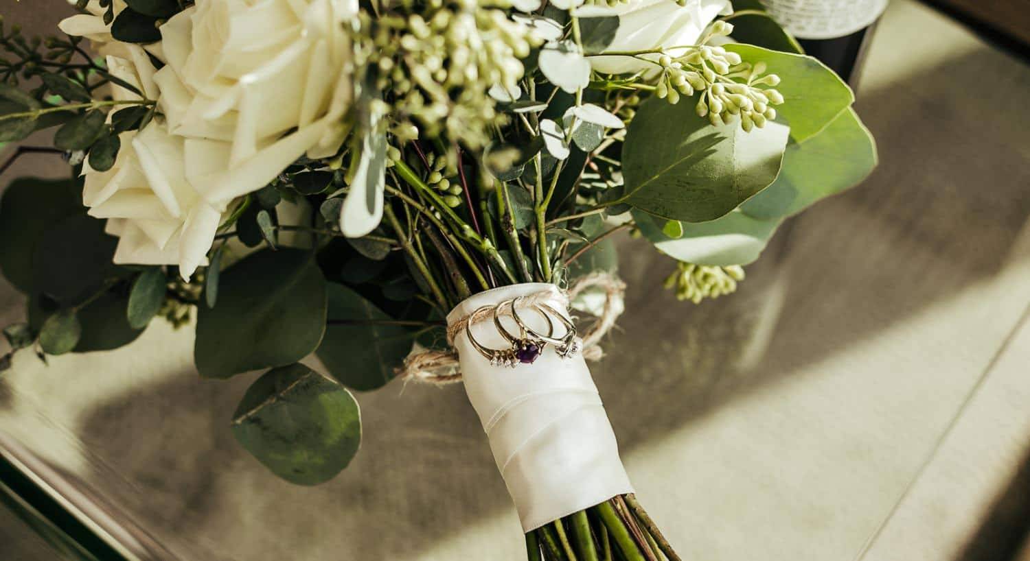 Bouquet of white flowers tied together with white fabric and a piece of twine holding three rings